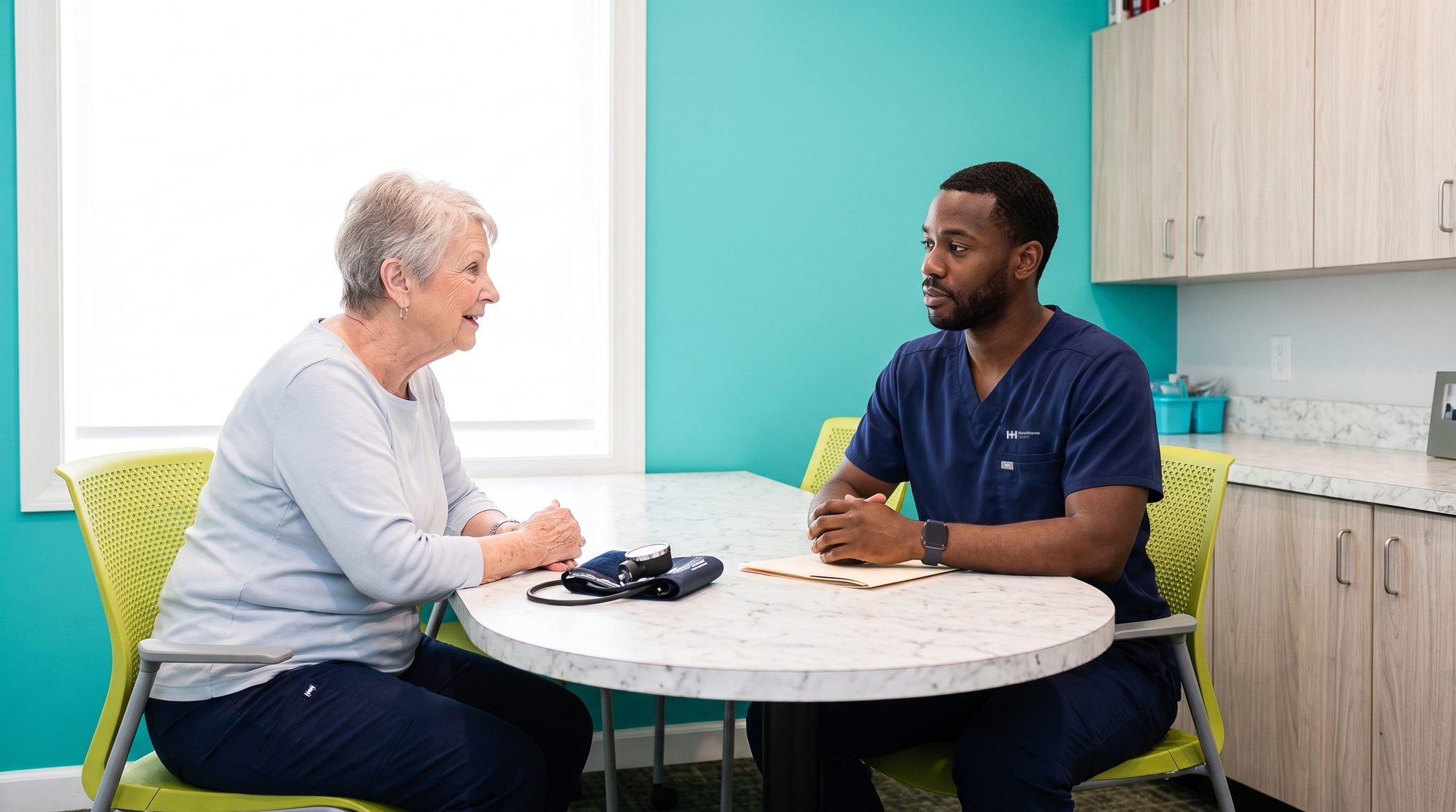 Research nurse talking with a patient at the consultation room table, blood pressure cuff on the table