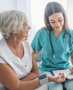 Older person is having blood pressure checked Nurse measuring blood pressure of senior woman at home. Smiling to each other. Young nurse measuring blood pressure of elderly woman at home. Doctor checking elderly woman's blood pressure