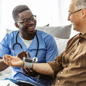 African-American Male Nurse Measuring Blood Pressure of Mature Patient in the Livingroom.